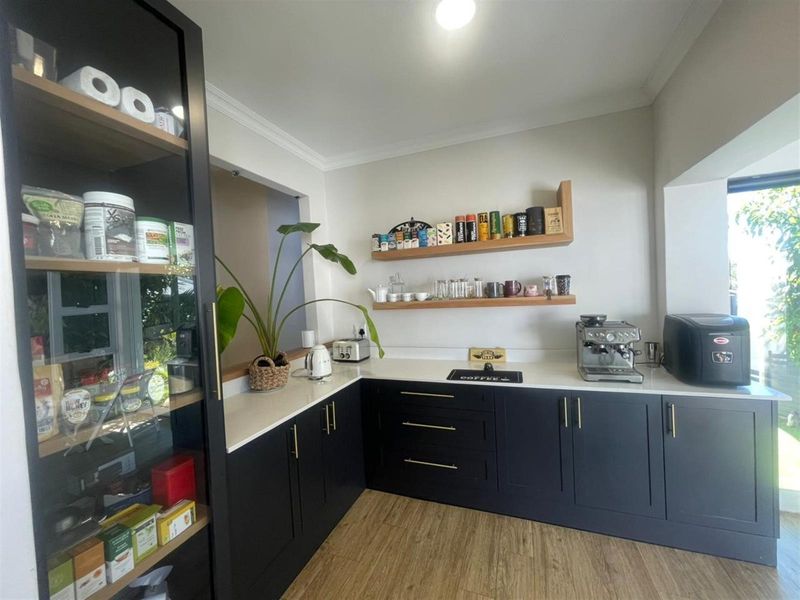 Modern kitchen featuring dark cabinetry, light stone countertops, floating timber shelves, and wood-look flooring, creating a clean and contemporary culinary space.