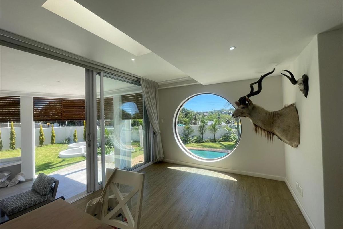 Bright living area featuring a unique circular window, recessed ceiling lighting, and large sliding glass doors opening onto a landscaped garden and pool area.