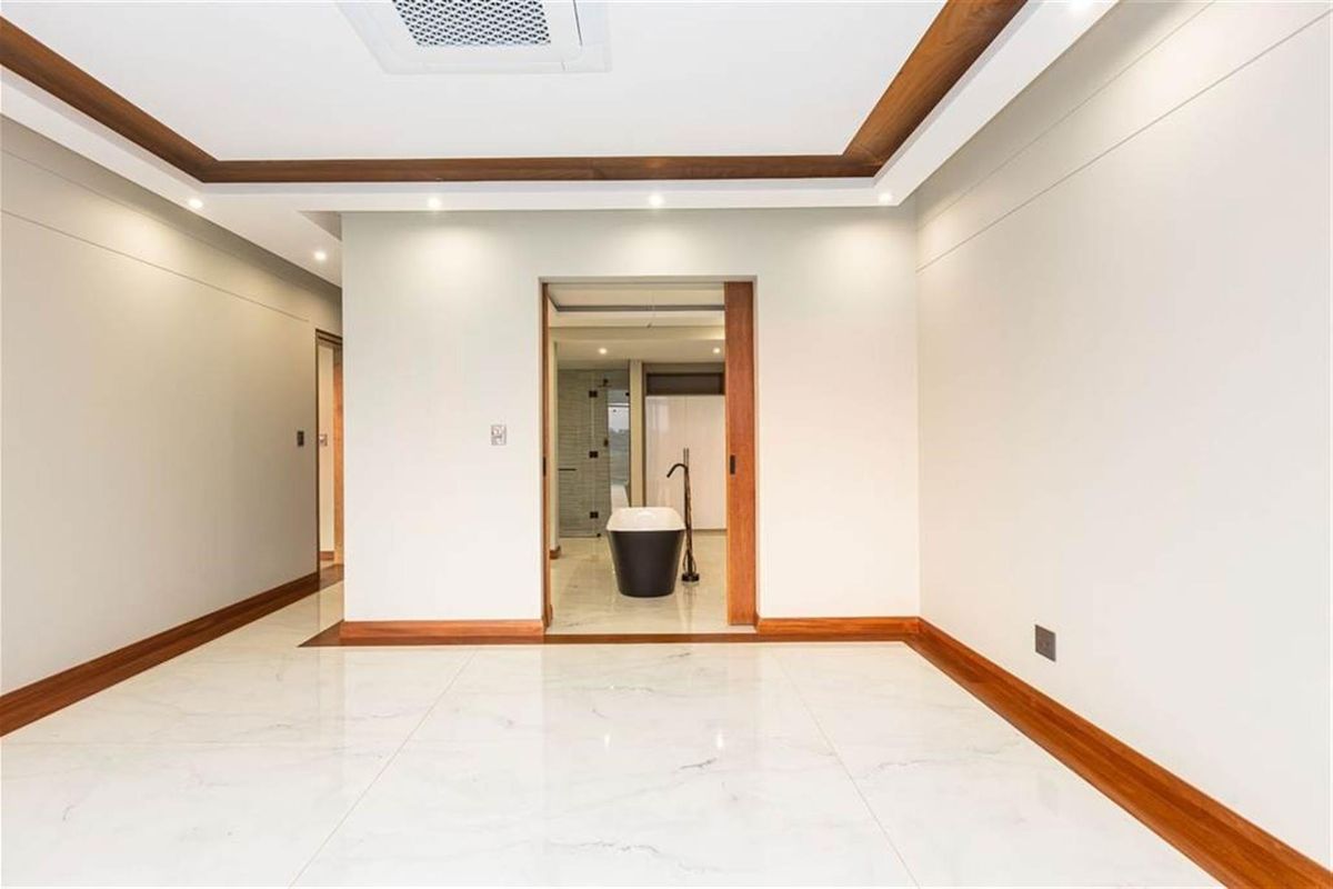A modern, well-finished room featuring polished marble-style flooring, timber skirting boards, and a recessed ceiling with integrated lighting, leading into an en-suite bathroom.