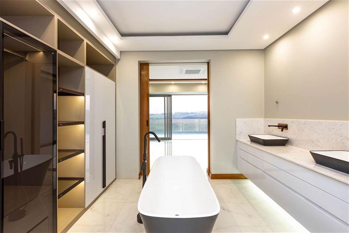 Modern primary bathroom featuring a freestanding bathtub, dual vessel sinks on a floating vanity, and integrated cabinetry with recessed lighting.