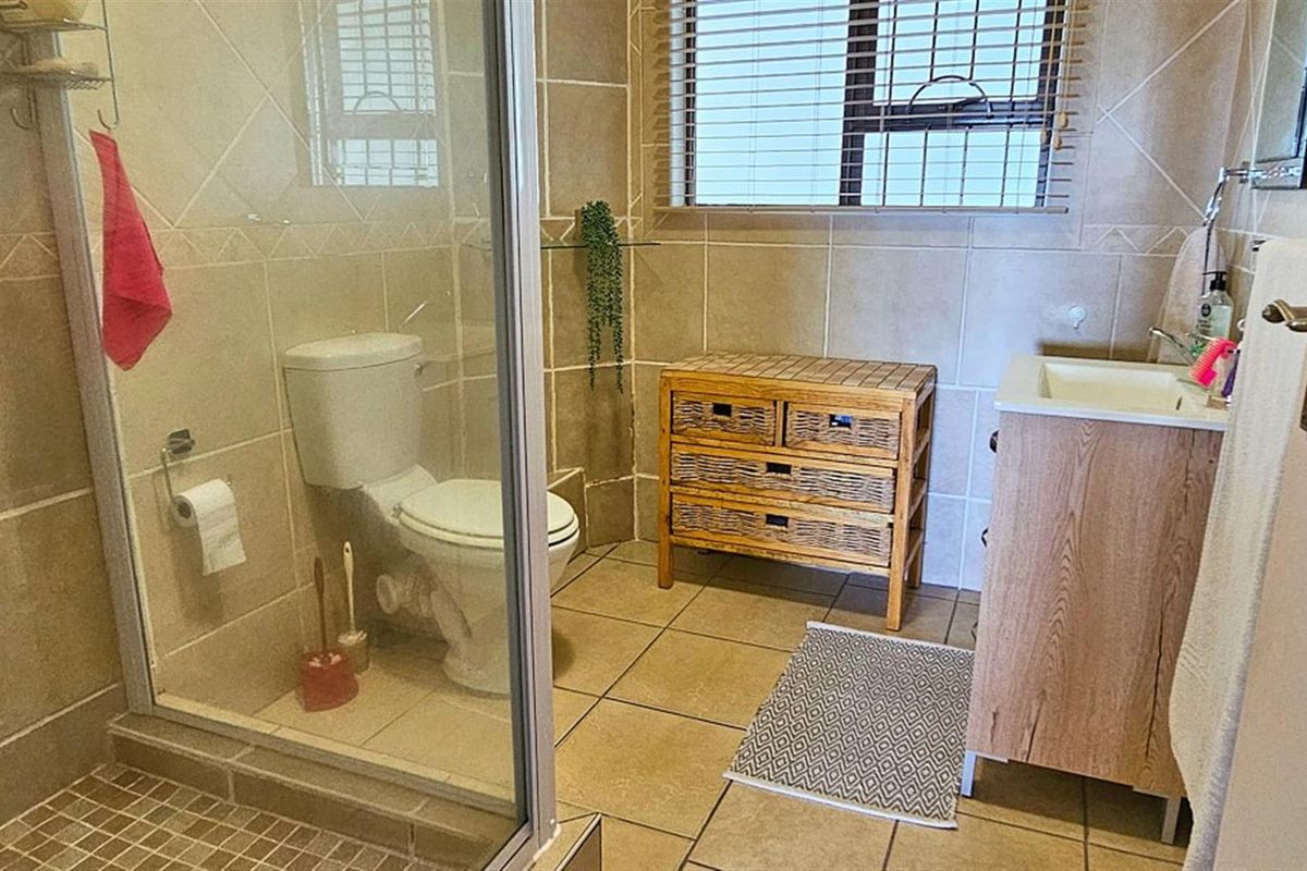 A functional bathroom featuring a glass-enclosed shower, tiled walls and flooring, a vanity basin, and a toilet.