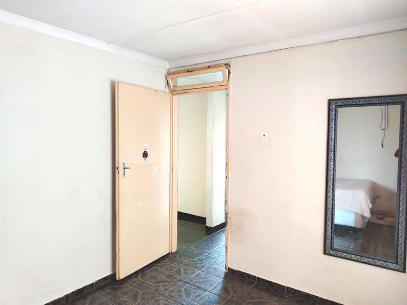 A simple bedroom interior featuring tiled flooring, a standard door with a transom window, and neutral wall finishes.