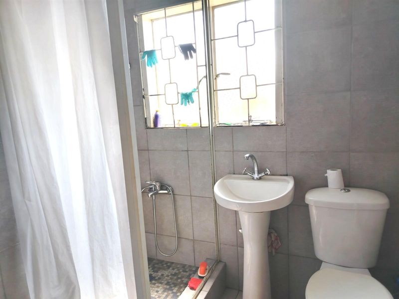 A functional bathroom featuring a pedestal basin, toilet, and shower area with tiled walls and security bars on the window.