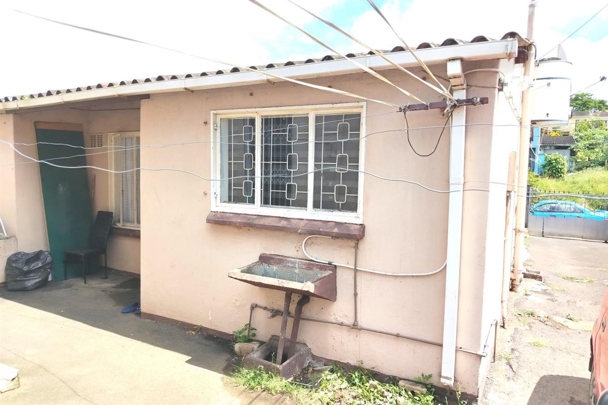 Rear exterior view of the property featuring a concrete apron, security-barred window, and an external utility sink with visible signs of wear.