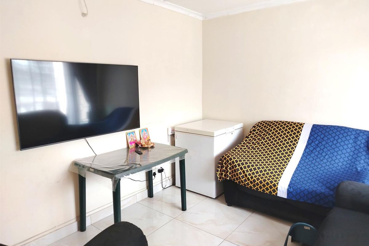 A living room featuring tiled flooring and a wall-mounted television, with basic finishes and visible electrical wiring.