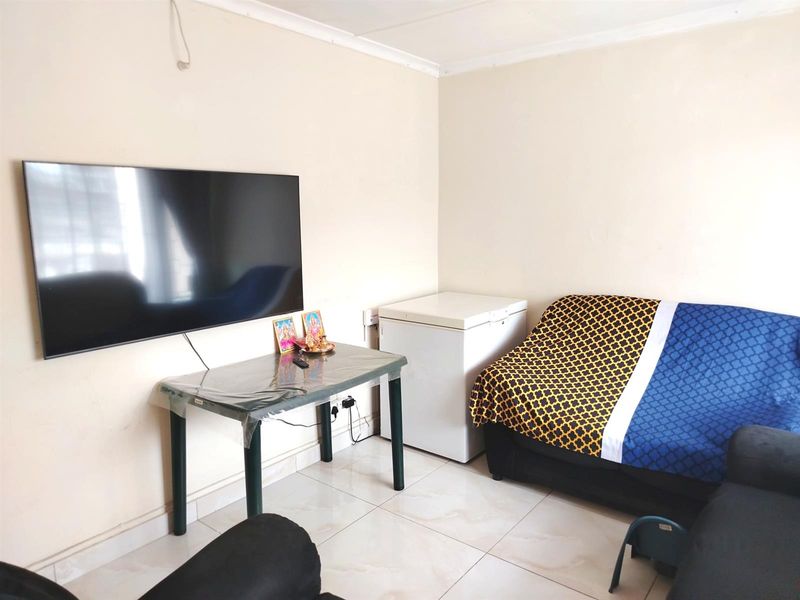 A living room featuring tiled flooring and a wall-mounted television, with basic finishes and visible electrical wiring.