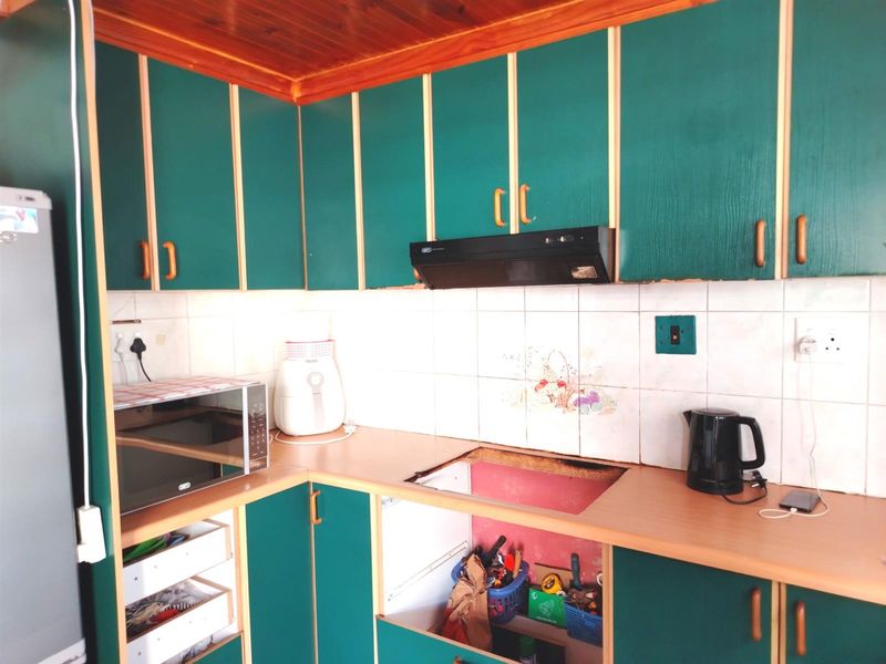 A kitchen featuring green cabinetry, timber ceiling, and tiled backsplash, currently requiring a new cooktop installation and general cosmetic updates.