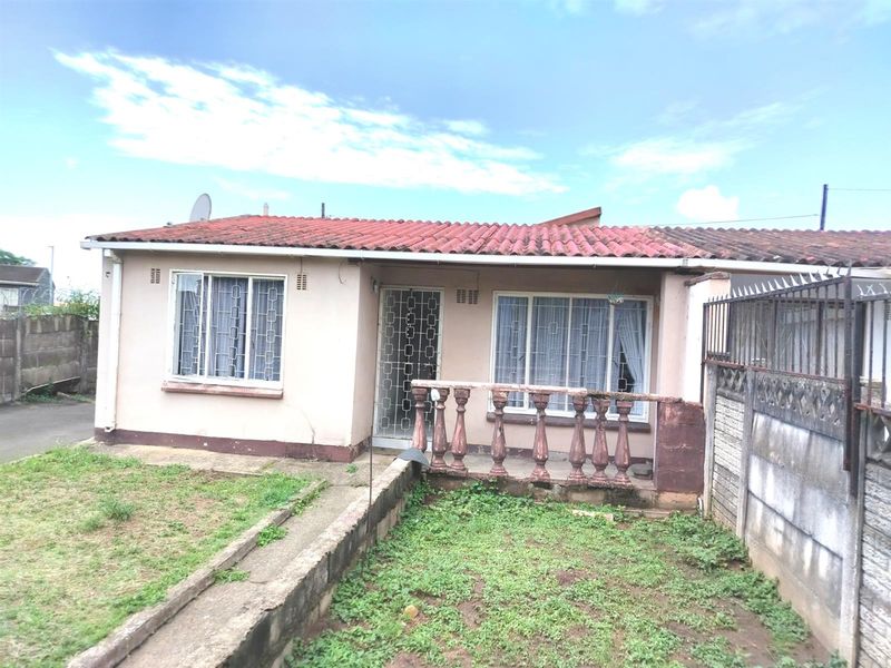 Front view of a single-story house featuring a terracotta tiled roof, security gate, and a small front garden with a concrete walkway.
