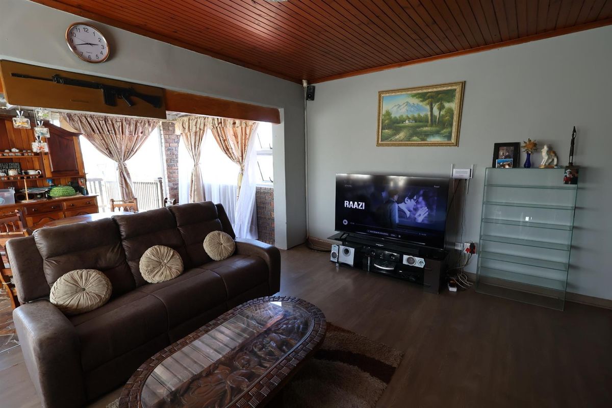 A spacious living room featuring a timber-paneled ceiling, laminate flooring, and an open-plan layout connecting to the adjacent dining area.