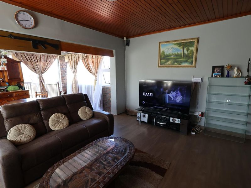 A spacious living room featuring a timber-paneled ceiling, laminate flooring, and an open-plan layout connecting to the adjacent dining area.