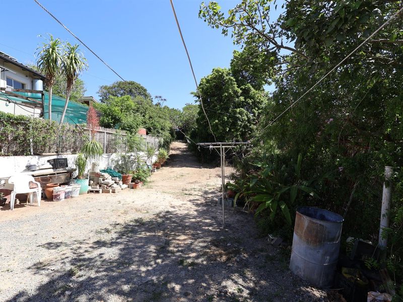 A rear outdoor area featuring a gravel pathway, established trees, and a boundary wall, providing a functional space for garden access.