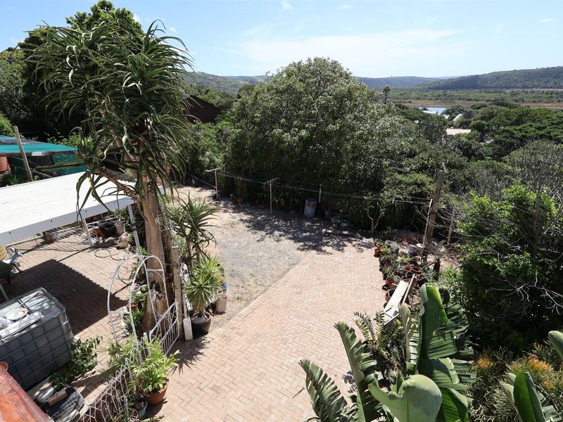 Elevated view of a paved backyard area featuring a covered patio structure, mature landscaping, and scenic natural surroundings.