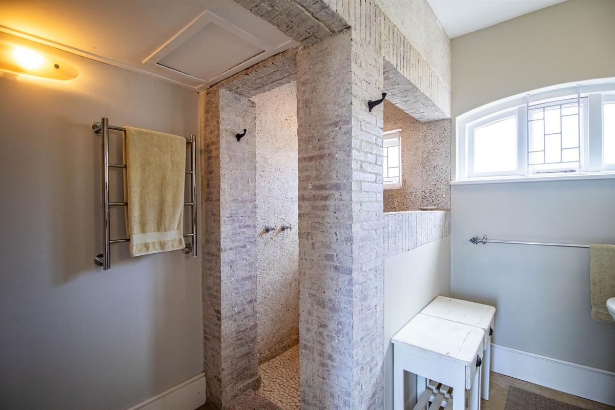 A bathroom featuring a unique exposed brick shower enclosure with a pebble floor, complemented by a wall-mounted heated towel rail and arched window.