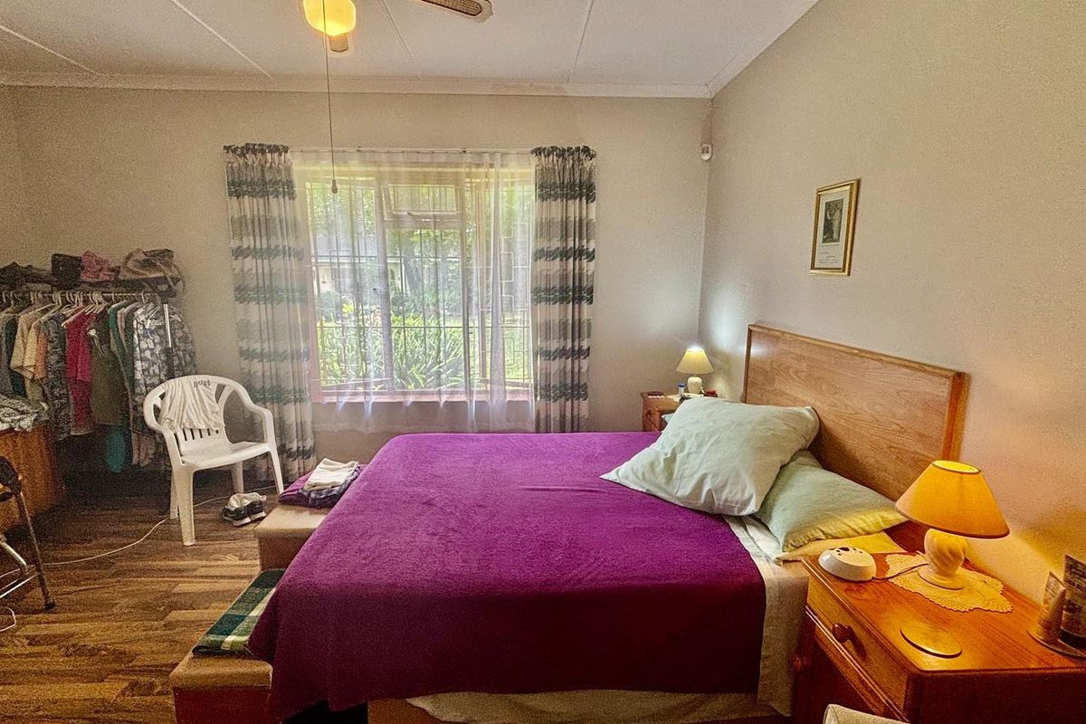 A bedroom featuring wood-look flooring, a large window with curtains, and a ceiling fan.