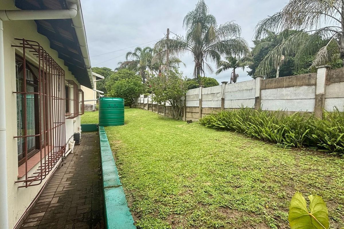 A spacious rear garden area featuring a paved walkway, a green water storage tank, and a long concrete boundary wall.