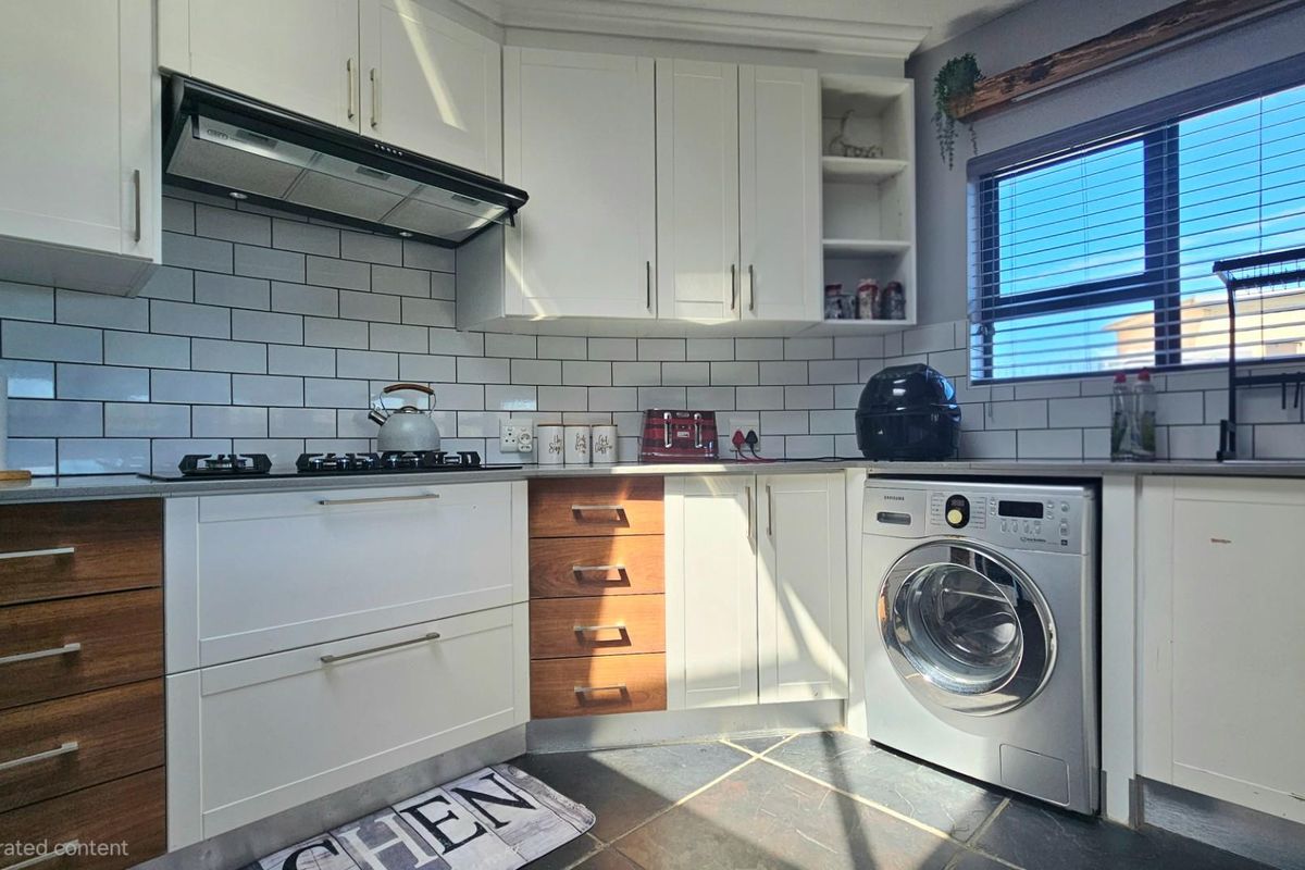 Modern kitchen featuring white cabinetry with wood-tone accents, subway tile backsplash, integrated gas hob, extractor fan, and built-in laundry appliance space.