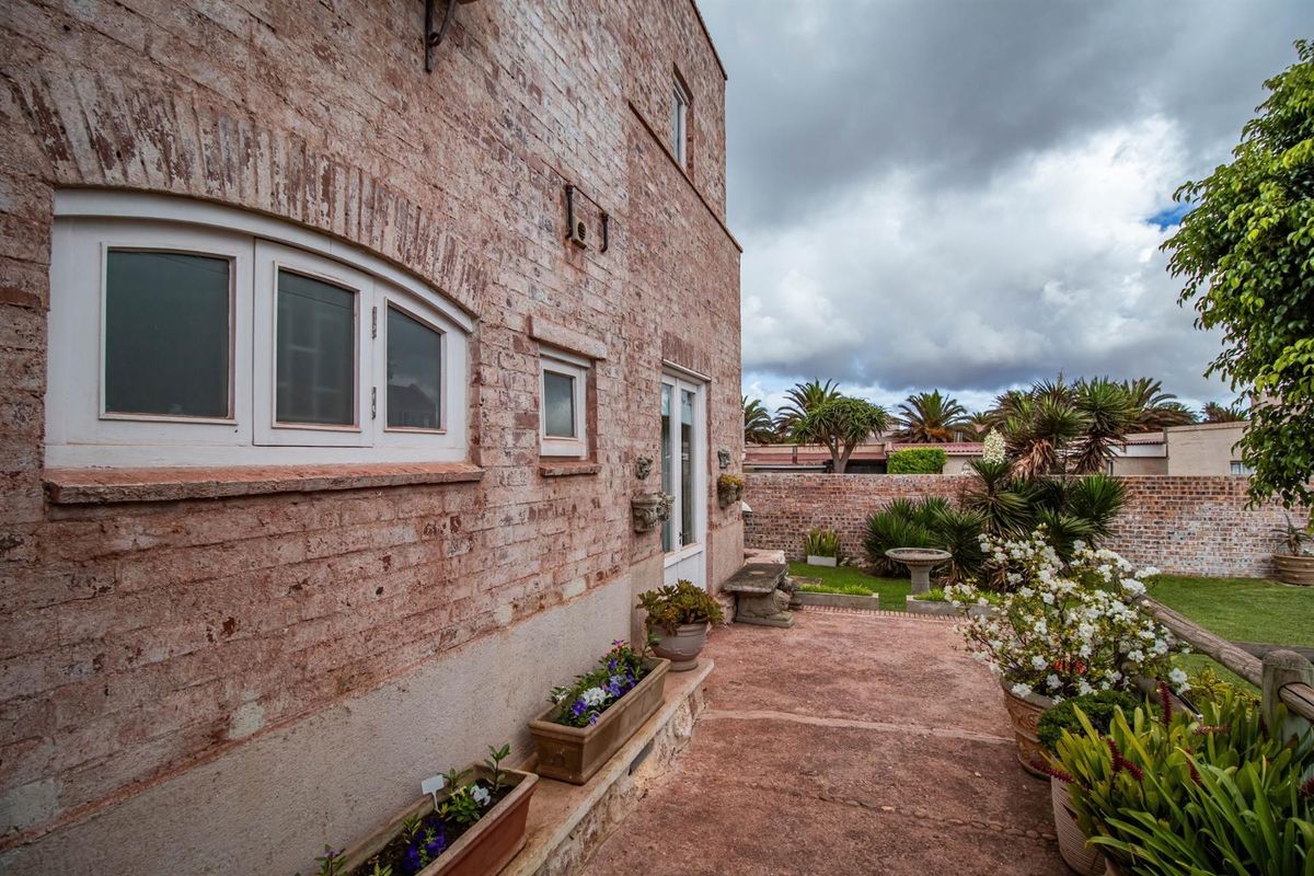 A view of the rear exterior facade featuring exposed brickwork, a paved patio area, and a well-maintained garden with perimeter walling.