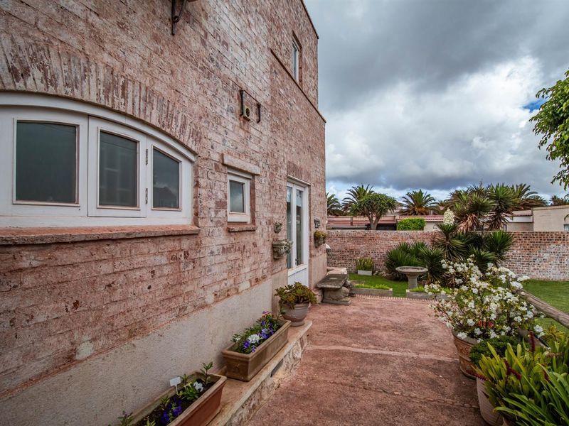 A view of the rear exterior facade featuring exposed brickwork, a paved patio area, and a well-maintained garden with perimeter walling.