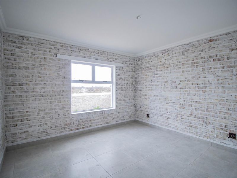 A bright, vacant bedroom featuring modern light-toned tiled flooring and distinctive whitewashed brick-style feature walls with a large window.