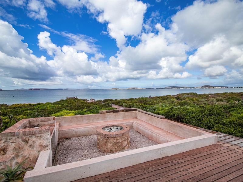 Outdoor entertainment area featuring a built-in stone fire pit and bench seating, overlooking the ocean and coastal landscape.