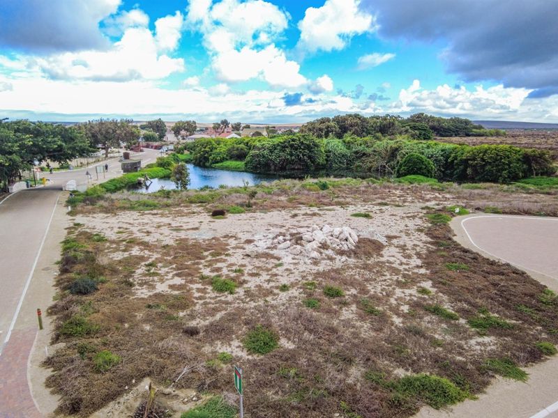 An elevated aerial view of a vacant residential plot featuring natural vegetation, adjacent to a small pond and local street infrastructure.