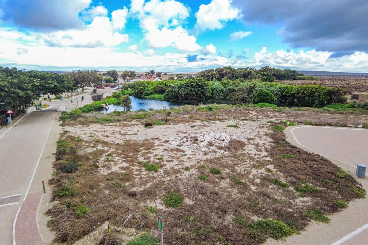 An elevated aerial view of a vacant residential plot featuring natural vegetation, adjacent to a small pond and local street infrastructure.