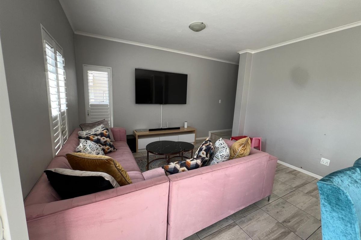 A comfortable living room featuring tiled flooring, plantation shutters, and a wall-mounted television setup.