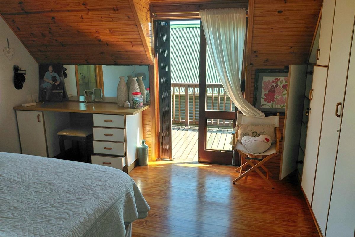 A cozy bedroom featuring warm timber-paneled walls and ceiling, built-in vanity cabinetry, and direct access to a private balcony through a glass door.