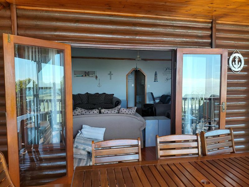 A view from a covered wooden patio looking into the living area through large glass double doors, featuring log-style exterior wall cladding.