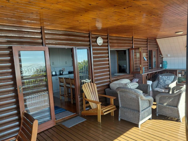 A covered timber patio featuring log-style wall cladding and wooden decking, providing direct access to the kitchen area.