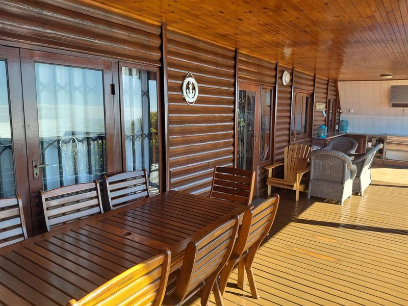 Spacious covered patio featuring timber log-style wall cladding, wooden decking, and a built-in outdoor kitchen area with tiled splashback.