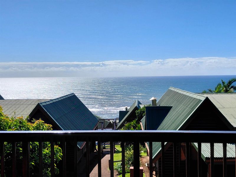 A scenic elevated view overlooking the ocean, featuring the pitched metal roofs of surrounding townhouse units and lush greenery.