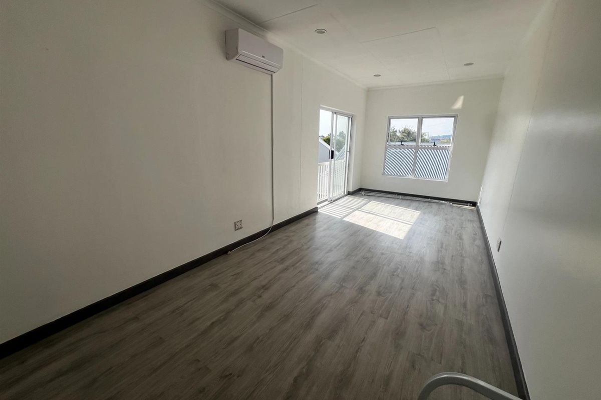 A bright, empty bedroom featuring modern wood-look flooring, recessed ceiling lighting, a wall-mounted air conditioning unit, and access to a balcony through sliding doors.