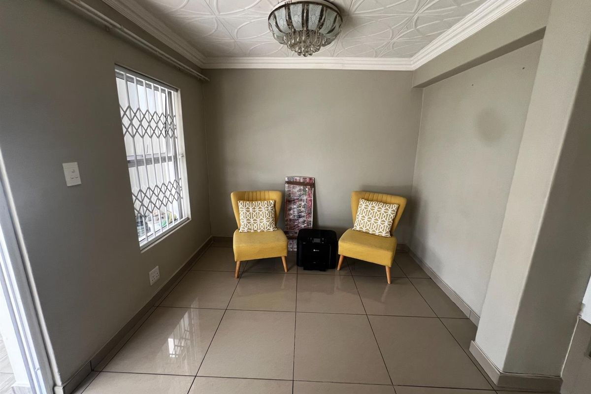A bright living area featuring large format floor tiles, decorative ceiling molding, and a security gate on the window.