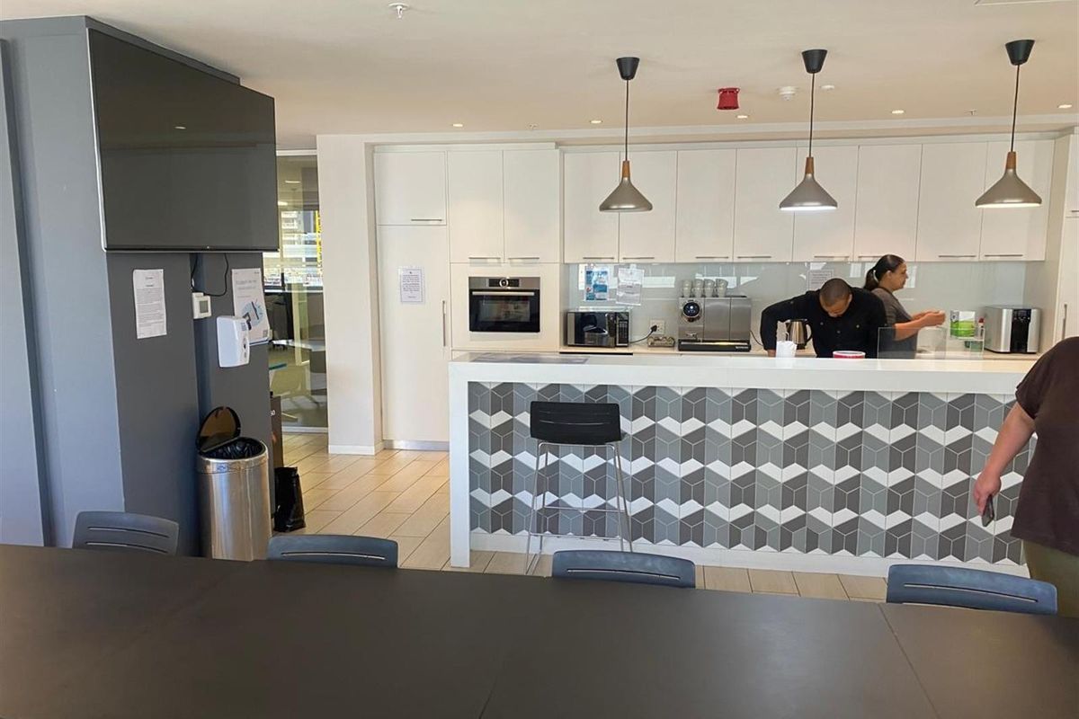 Modern office kitchenette featuring white cabinetry, a geometric tiled breakfast bar, built-in oven, and pendant lighting in a professional workspace setting.