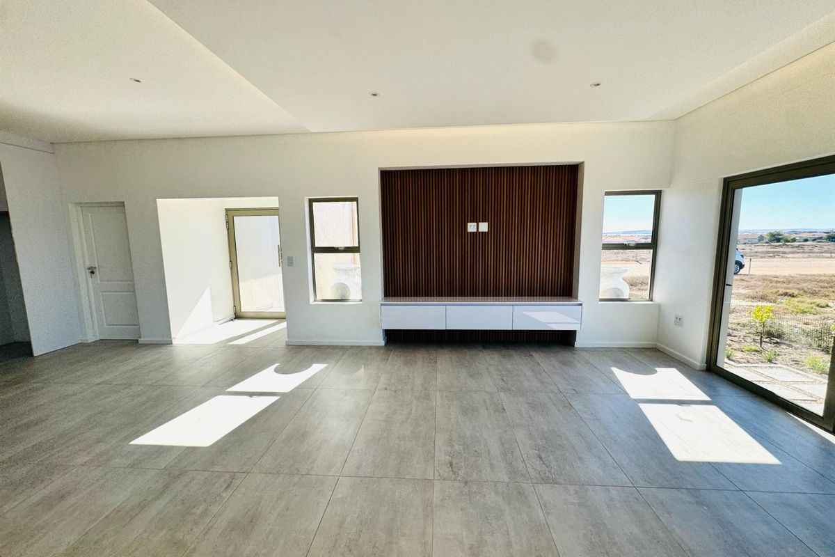 Spacious living area featuring modern wood-slat feature wall, built-in media console, large format floor tiles, and sliding glass doors leading to the exterior.
