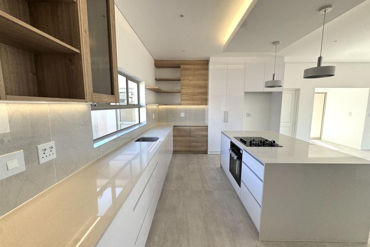 Modern kitchen featuring a central island with a built-in hob and oven, sleek cabinetry, stone countertops, and integrated under-cabinet lighting.