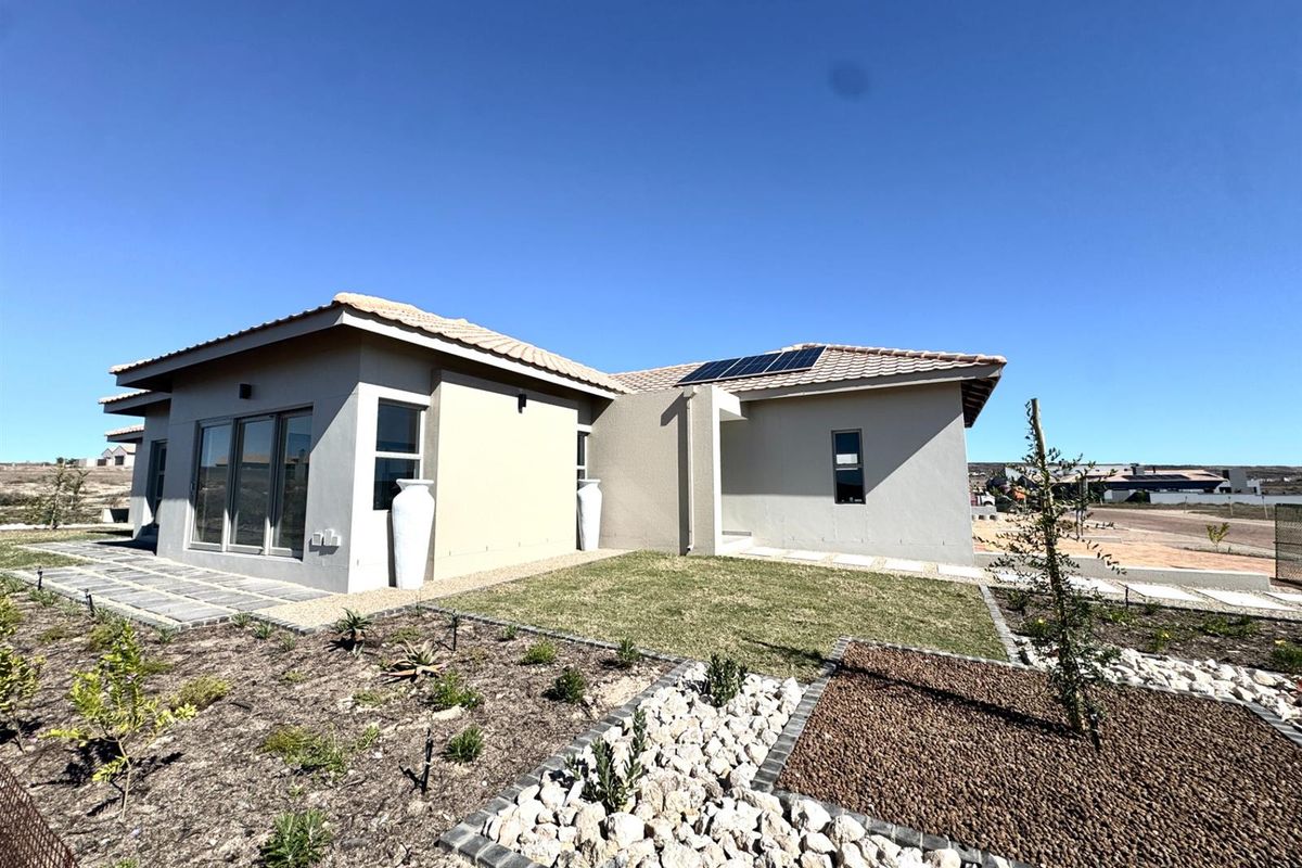 A modern single-story residence featuring a tiled roof, solar panels, and a landscaped garden with stone accents and paved walkways.