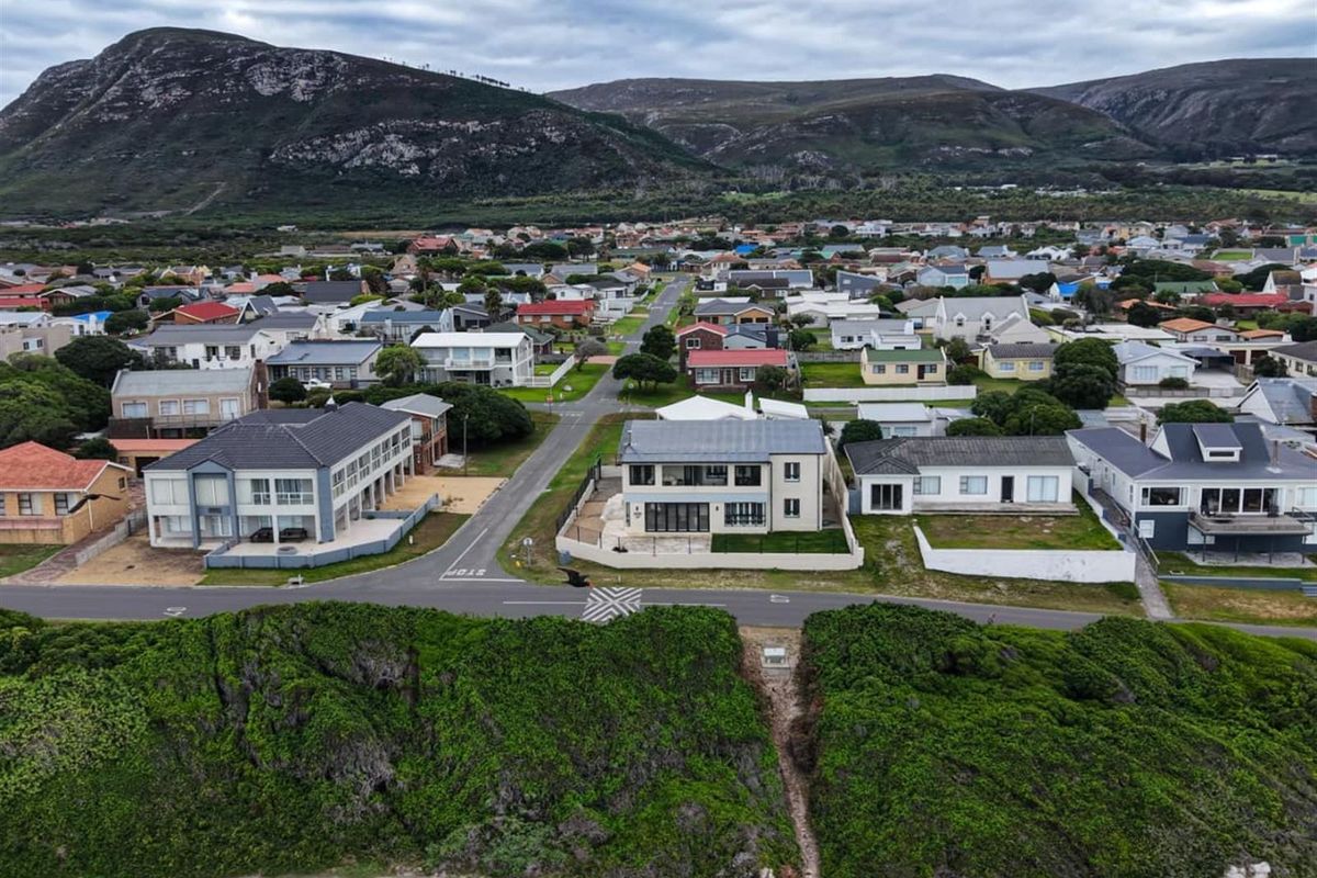 Aerial view of the property situated in a coastal residential neighborhood, showcasing its proximity to the coastline and surrounding mountain landscape.