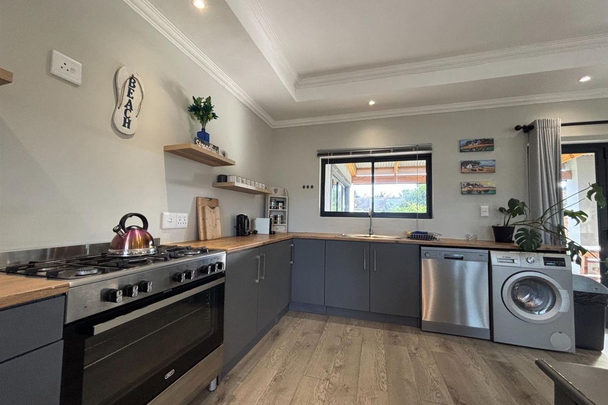 Modern kitchen featuring dark grey cabinetry, wooden countertops, a gas stove, and integrated laundry appliances, with a clean, contemporary aesthetic.