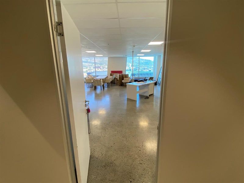 Open-plan office space featuring polished concrete flooring, recessed ceiling lighting, and large windows offering expansive city and mountain views.