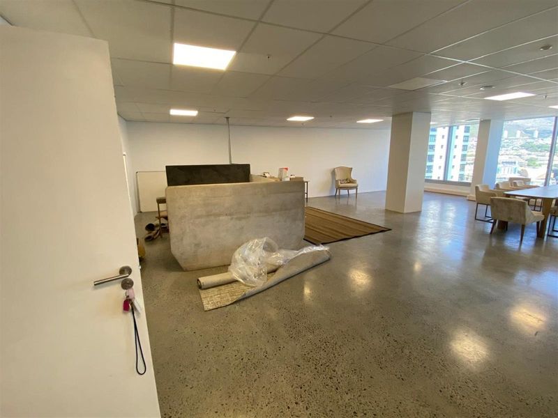 Spacious open-plan office area featuring polished concrete floors, recessed ceiling lighting, and large windows providing ample natural light and city views.