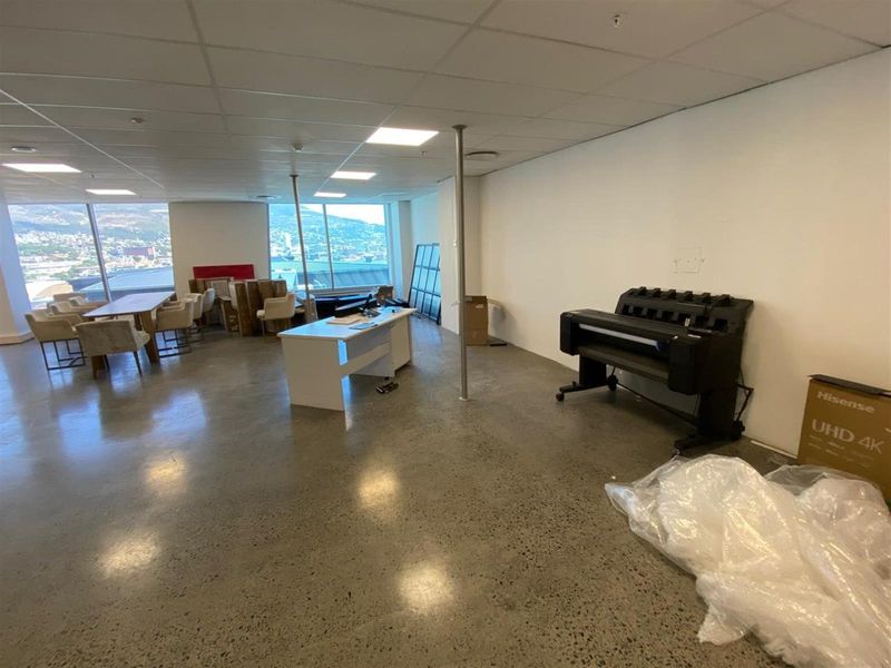 Open-plan office space featuring polished concrete flooring, suspended ceiling tiles, and large windows offering expansive city and mountain views.