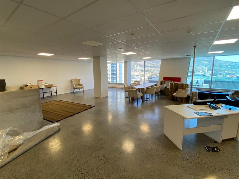 Spacious open-plan office area featuring polished concrete floors, suspended ceiling tiles, and large floor-to-ceiling windows with expansive city and mountain views.
