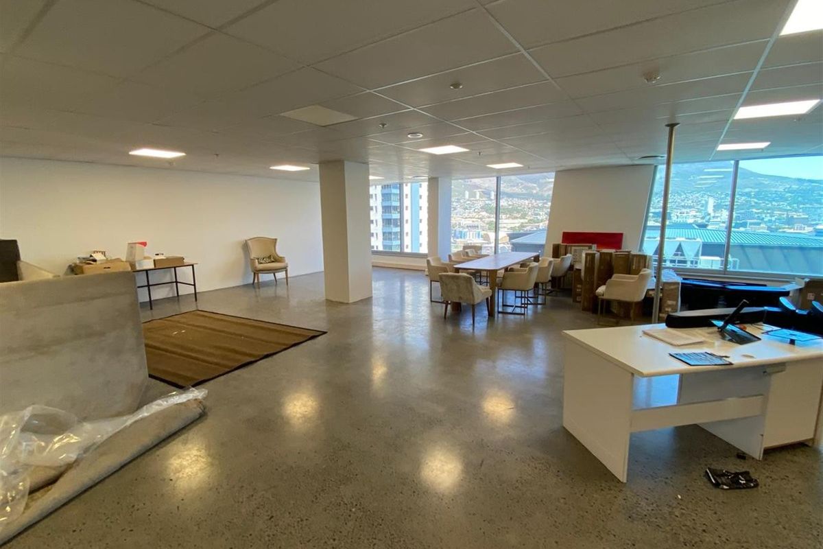 Spacious open-plan office area featuring polished concrete floors, suspended ceiling tiles, and large floor-to-ceiling windows with expansive city and mountain views.