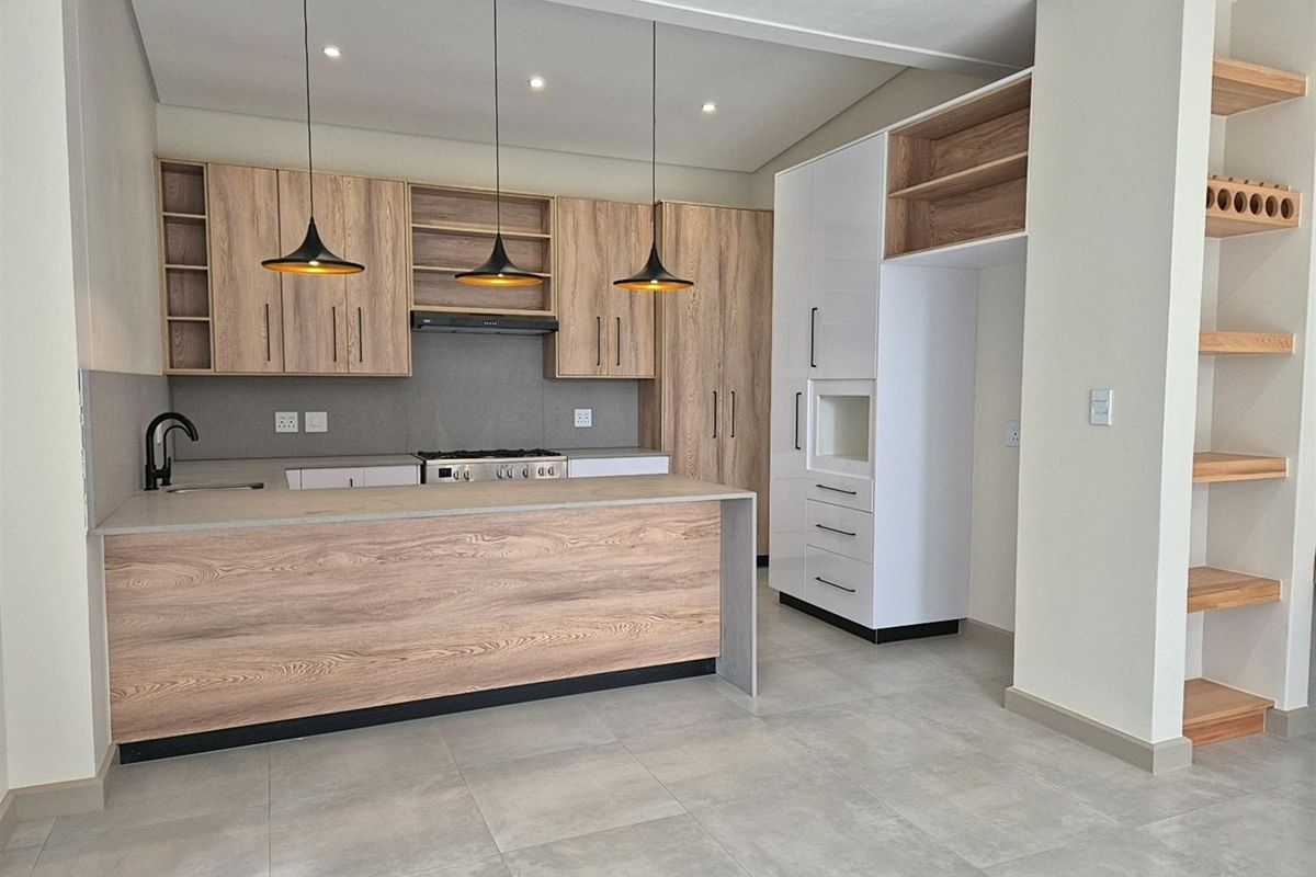 Modern kitchen featuring wood-grain cabinetry, stone countertops, integrated oven and hob, and stylish pendant lighting with open shelving and tiled flooring.