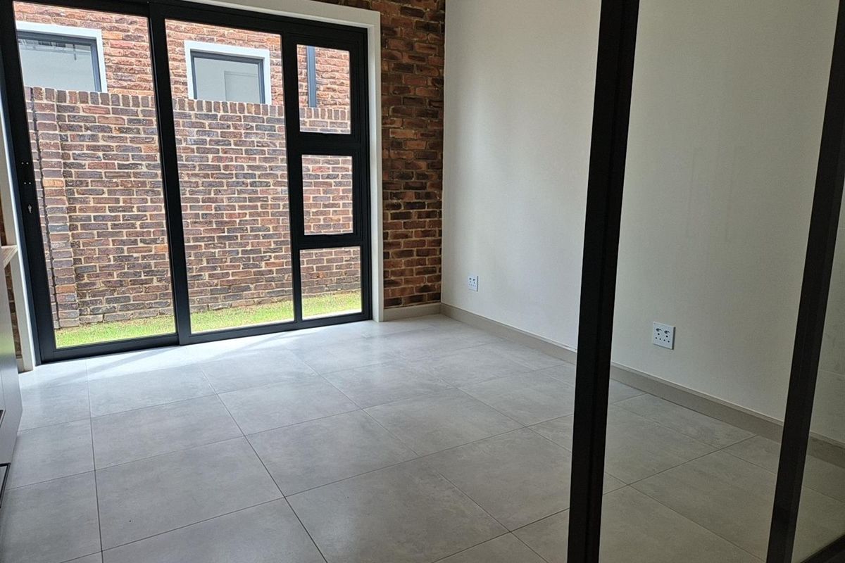 A bright, modern room featuring large black-framed sliding glass doors, exposed brick accent wall, and neutral floor tiling.