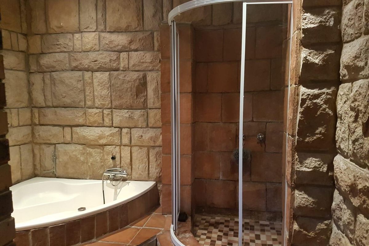 Bathroom featuring a corner bathtub and a separate shower enclosure with rustic stone-clad walls and tiled flooring.
