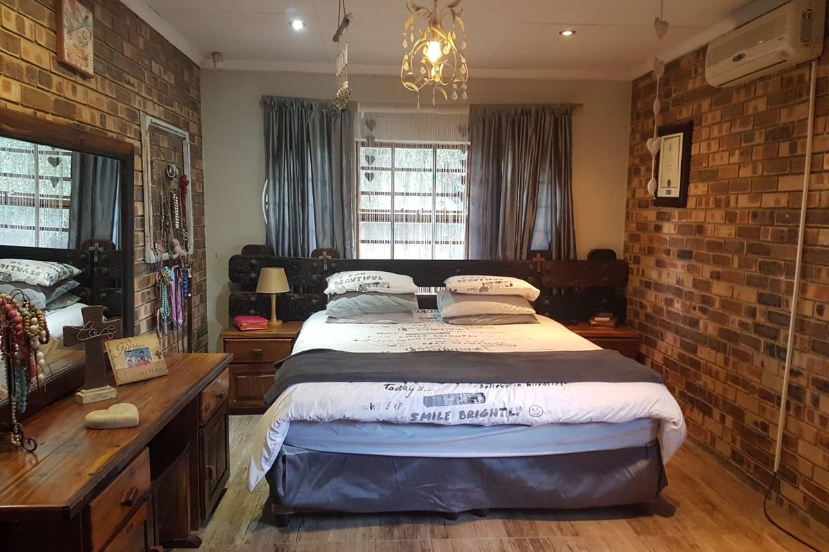 A bedroom featuring exposed brick feature walls, wood-look flooring, and a wall-mounted air conditioning unit.