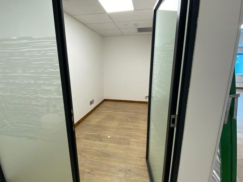 A clean, empty office space featuring modern glass-paneled doors, wood-look flooring, and a drop ceiling with integrated lighting.